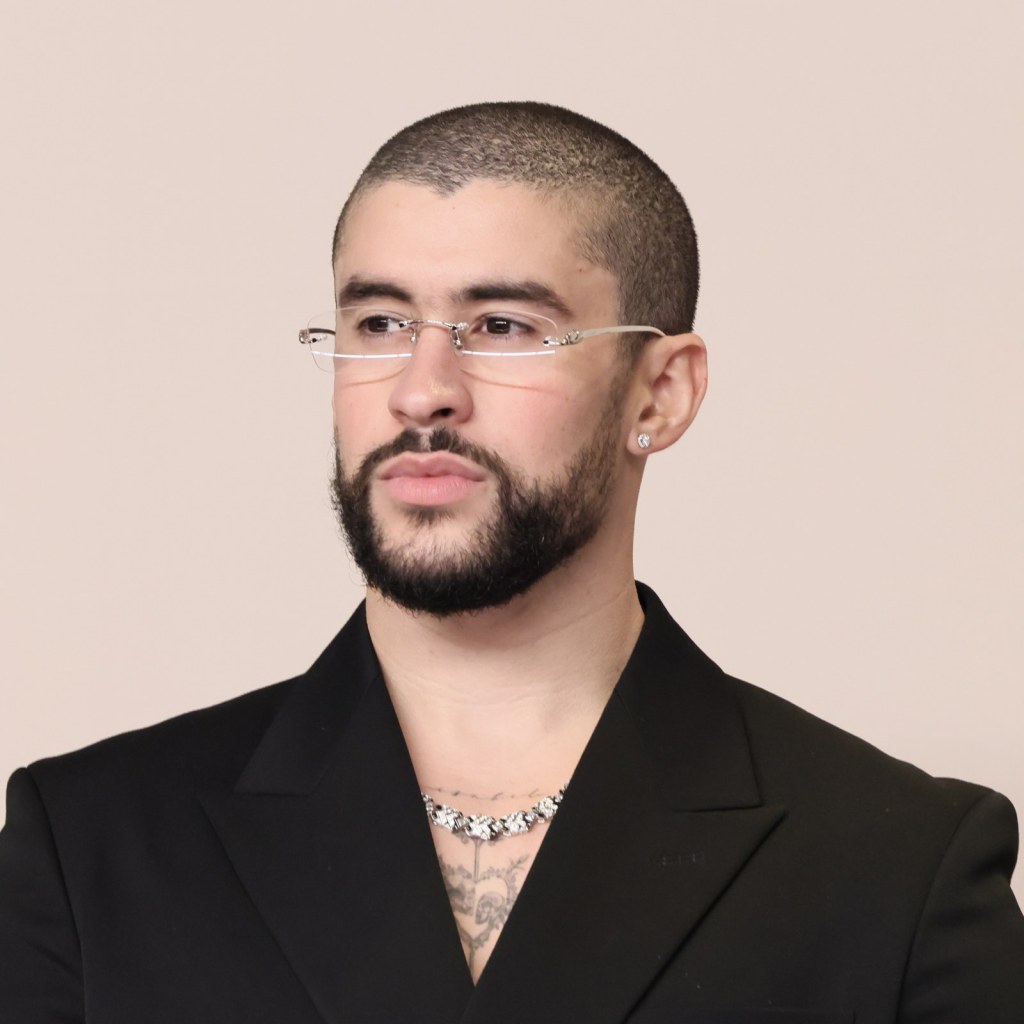 Un homme avec une coupe buzz cut élégante, une barbe bien taillée et des lunettes de style moderne.