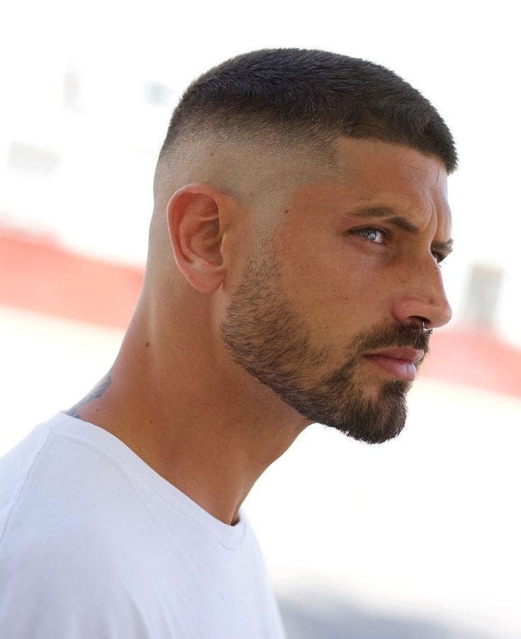 Homme avec une coupe buzz cut dégradée, arborant une barbe soignée et un style épuré.
